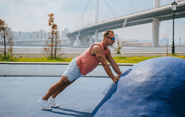 A professional athlete trains outdoors, does push-ups to get dressed, sportswear, sunglasses on the background of the big bridge of the city. Sports fitness healthy lifestyle