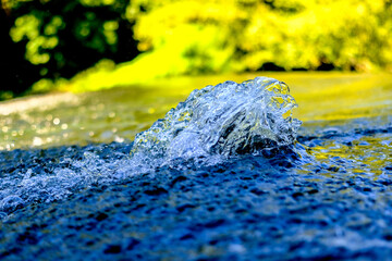 Water droplets / watercourse with reflections in the sunlight. Wonderful play of colours in small drops of water in a stream in the sun. Close-up taken in sunshine on the bank.