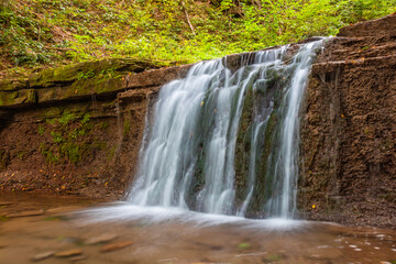 Fototapeta na wymiar Scenic waterfall in a mountain stream in the forest. One of the waterfalls of the cascade of Rusiliv waterfalls. Rusyliv, Ternopil Region, Ukraine