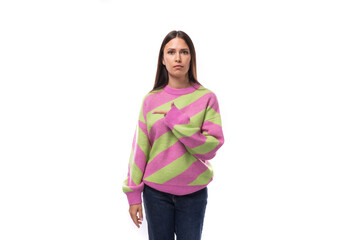 well-groomed slim young european brunette woman dressed in a striped pink-green pullover on a studio background