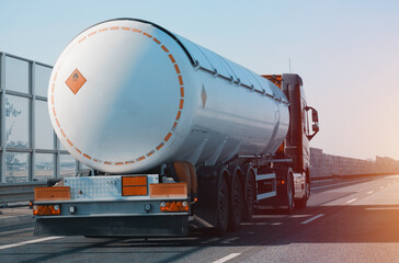 Petroleum Cargo Truck Driving On The Highway Hauling Oil Products. Fuel Delivery Transportation And Logistics Concept On A Sunny Summer Evening. Compressed Gas Carrier Truck Rear View On A Highway.