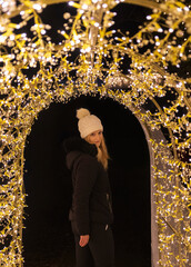 Portrait of beauty young woman in white hat and black jacket posing on tunnel made from decoration light. People outdoor photo