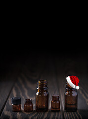 Santa Claus hat on bottle with essential oil on wooden table. Variuos dark glass jars for...