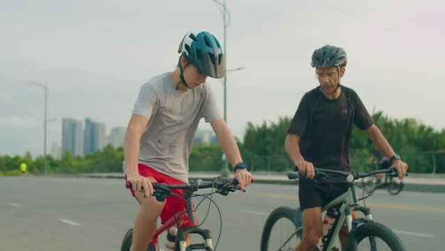 Father and teen son cycling along road, taking break and drinking water during bike ride on summer day