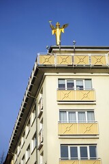 Goldene Figur eines Engel vor blauem Himmel im Sonnenschein auf einem sanierten Wohnhaus der Nachkriegszeit mit Apotheke in Gießen an der Lahn in Hessen