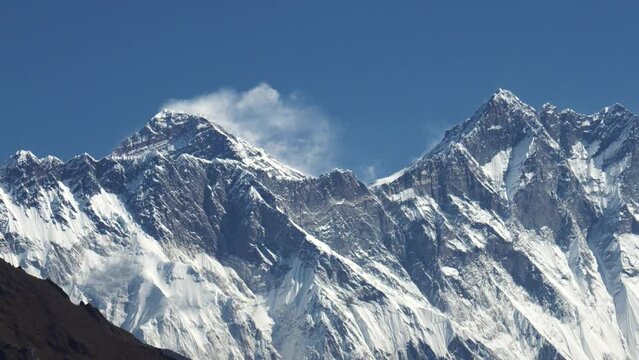 Snow covered Mount Everest rises above barren landscape of Himalayan Mountains. View of Mount Everest and Lhotse. Strong wind at top forms snow flag. Trekking in Nepal and highest mountains in world