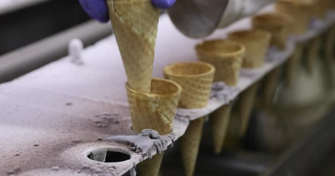 Food industry. Industrial ice cream factory line. Closeup view of an operator with gloves placing cones in the machine. 