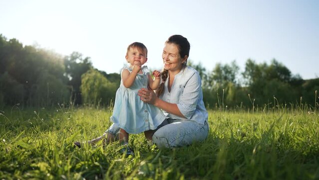 happy family. Mom with baby girl in tpark on green grass. Mom teaches daughter to walk. first steps of toddler daughter in summer park on green grass. Mom and daughter picnic in the park dream game.