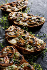 Toasts with  mushrooms and cheese with fresh thyme on a black background, focus on the  toast inside, close up view