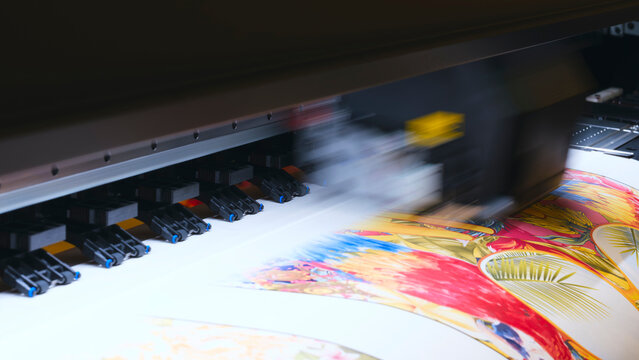 A moving working industrial wide format printer prints a color picture on paper.