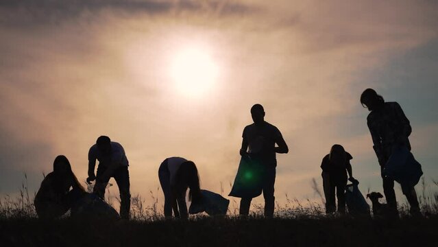 Teamwork.Silhouette of group of people clean up garbage at sunset in nature.Environmental pollution.Family cleaning plastic garbage in bag.People volunteers cleaning garbage in nature in summer park