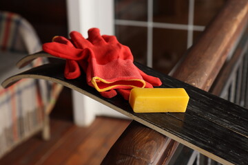 A block of yellow paraffin wax and red gloves on the black sliding surface of skis - obrazy, fototapety, plakaty