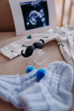 Gender neutral things during pregnancy or expecting a baby. Clear baby pacifier with tentacles, ultrasound photo, small blue knitted socks and bodysuit