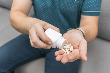 Man taking medicine from a bottle, holding white therapeutic capsules, antibiotics, vitamins, painkiller pills in a hand, close-up view - obrazy, fototapety, plakaty