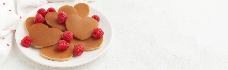 A heap of heart shaped pancakes with raspberries on the white plate on the white background