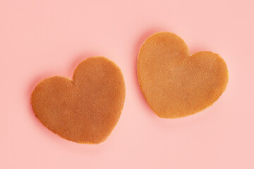 Close up top view of two heart shaped pancakes on the pink background