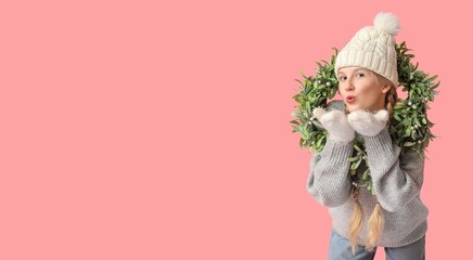 Pretty young girl with Christmas wreath blowing kiss on pink background with space for text