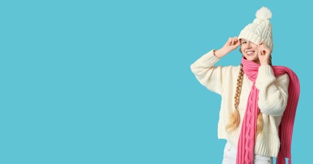 Pretty young girl in warm winter clothes on light blue background with space for text