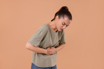 Woman suffering from abdominal pain on beige background. Unhealthy stomach