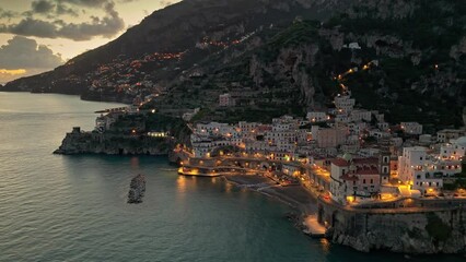 Flying above famous Amalfi Coast after sunset. Small beautiful coastal towns - Atrani and Amalfi with city lights. Amalfi coast near Naples, Campagna, Italy. High quality 4k