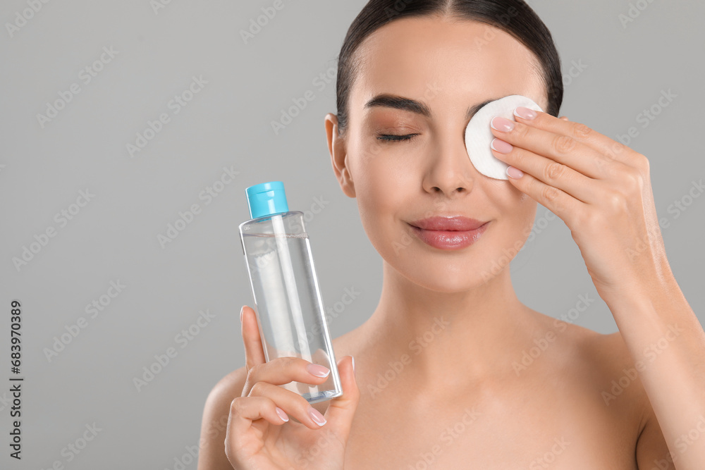 Wall mural Beautiful woman removing makeup with cotton pad on light grey background. Space for text