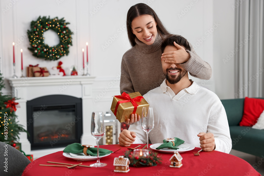 Poster Happy woman surprising her boyfriend with Christmas gift at home