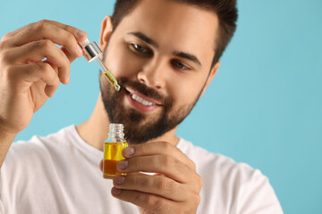 Handsome man with cosmetic serum in hands on light blue background, selective focus