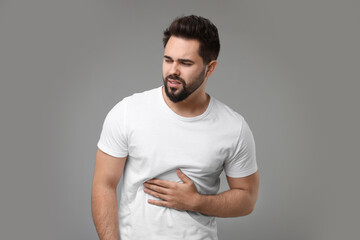Young man suffering from stomach pain on light grey background