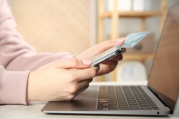 Fototapeta premium Online payment. Woman using credit card and smartphone near laptop at light grey table indoors, closeup