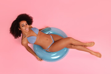 Beautiful woman in stylish bikini with inflatable ring on pink background, top view