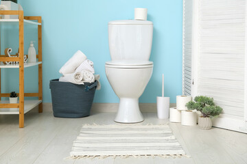Basket with clean towels and paper rolls on floor near toilet bowl