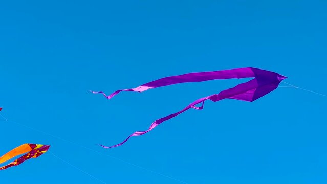 Colorful kites are flying in the blue sky and swaying in the wind during summer outdoor festival. Childhood, freedom and leisure time concept