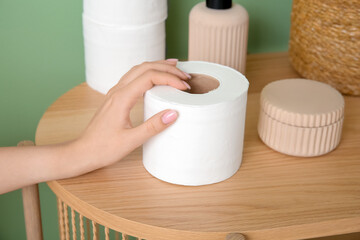 Woman taking toilet paper roll from wooden table against green wall