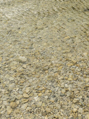 Traquil abstract background of pebbles under clear water. Ripple on a water surface. Beige color. Vertical format.