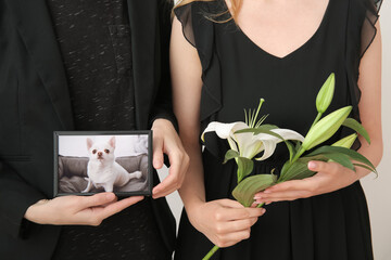 Women holding frame with picture of dog and lily flowers, closeup. Pet funeral