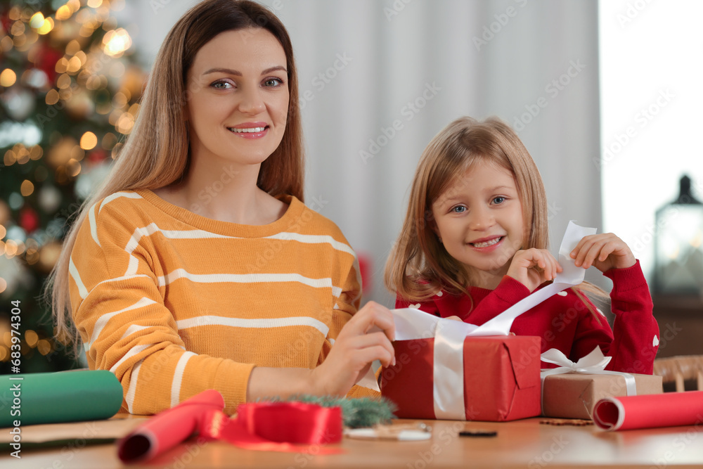 Wall mural Christmas presents wrapping. Mother and her little daughter decorating gift box with ribbon at home