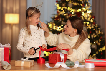 Fototapeta na wymiar Christmas presents wrapping. Mother and her little daughter decorating gift box with ribbon at home
