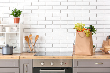 Paper bag with different products and utensils on counter in kitchen - obrazy, fototapety, plakaty