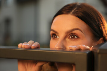 Concept of private life. Curious young woman spying on neighbours over fence outdoors, closeup