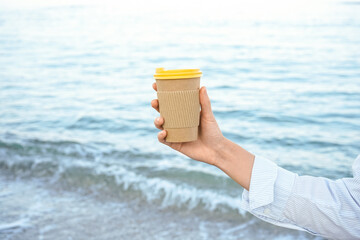 Woman holding paper coffee cup by the sea