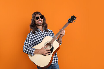 Hippie man in sunglasses playing guitar on orange background