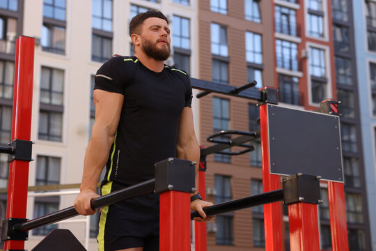 Man training on parallel bars at outdoor gym, low angle view