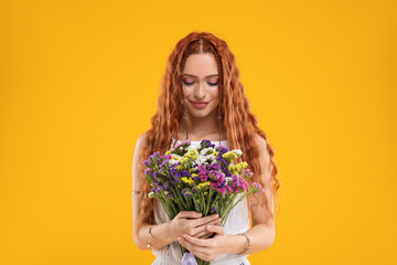 Beautiful young hippie woman with bouquet of colorful flowers on orange background