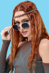 Stylish young hippie woman in sunglasses on light blue background