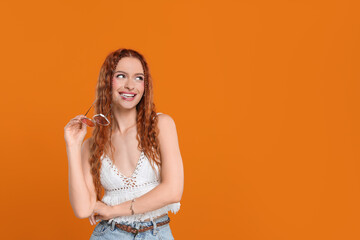 Stylish young hippie woman with sunglasses on orange background, space for text