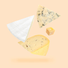 Different kinds of cheese falling on beige background