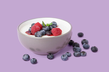 Bowl of tasty semolina porridge with fresh berries on lilac background