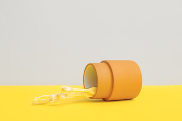 Yellow toothbrushes in orange holder on color background.
