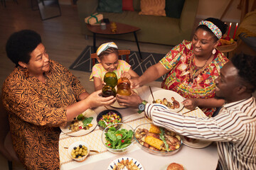Black family clinking glasses over dinner table celebrating Kwanza holiday