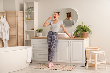 Beautiful young woman brushing teeth in bathroom
